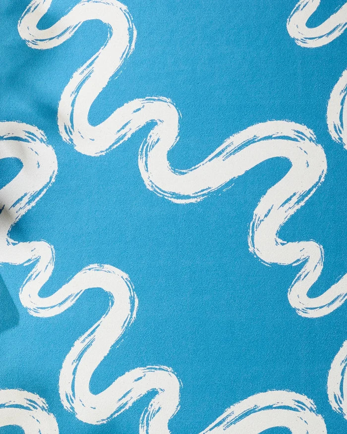 The "Go With the Flow" design by Elena Fay features a blue background with wavy, white brushstroke lines, inspired by the textured feel of a non-slip yoga towel.
