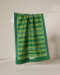 The GEOMETRY Goal tea towel features a green soccer field design with white markings and stripes, hanging from a string against a neutral backdrop.