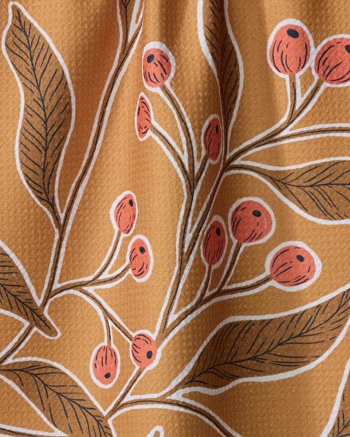 A close-up of Amy MacCready's Golden Berries tea towel shows dark green leaves and red-orange berries on a mustard yellow background. Made from ultra-absorbent, recycled materials, the fabric has a slightly textured feel.