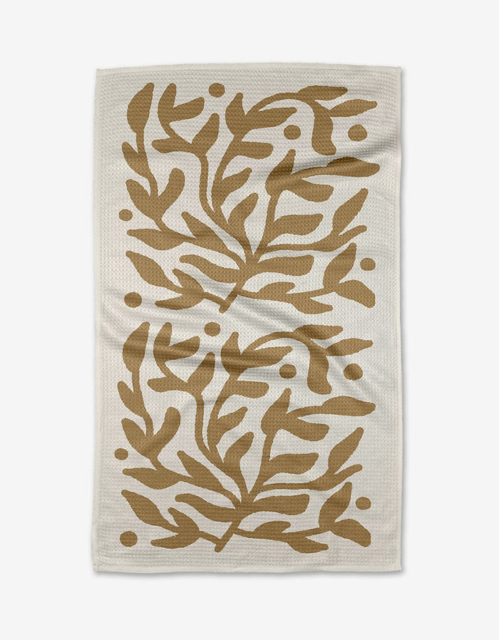 The Golden Garden tea towel by Graphics and Grain features a white, textured Geoweave fabric with symmetrical abstract brown leaves and dots in mirrored sections for durability and softness.