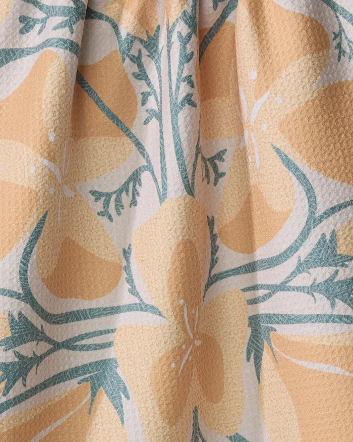 Close-up of Julianne Haness's "Golden Poppy" tea towel, showcasing a yellow and white floral design with green stems on a pale background. Made from quick-drying, recycled fabric, the material is slightly gathered at the top.