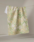 The Danelys Sidron "Golden Summer" towel, featuring a green, yellow, and white floral pattern, hangs on a clothesline against a neutral background.