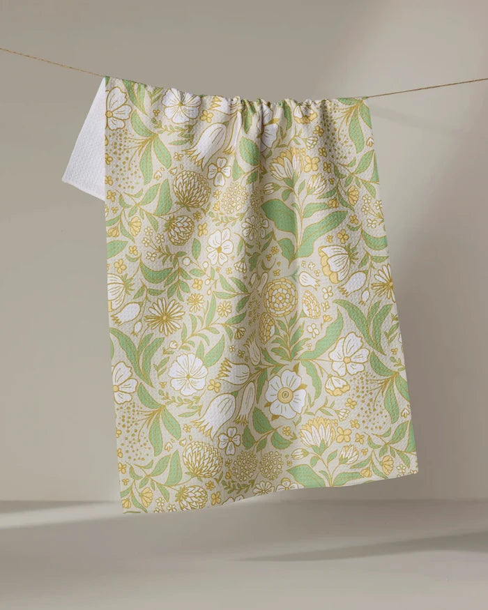 The Danelys Sidron "Golden Summer" towel, featuring a green, yellow, and white floral pattern, hangs on a clothesline against a neutral background.