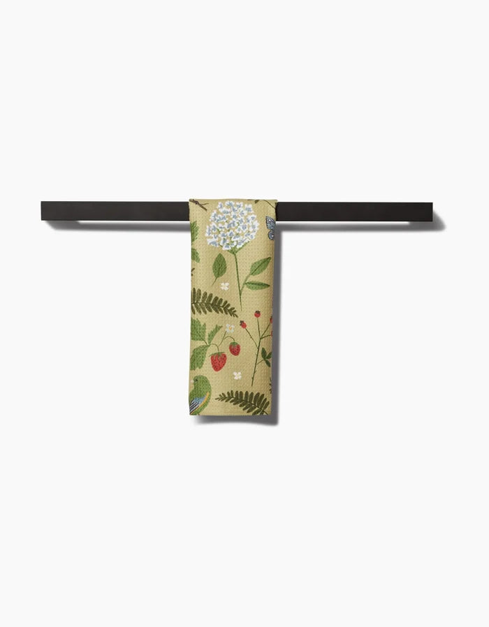 The Good Green Earth bar towel by Janna Sue Design features a botanical pattern and hangs on a sleek black bar. Crafted from Geoweave fabric, it stands out against the white background.