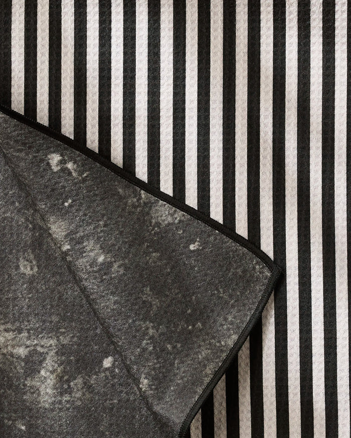 A close-up of Geometry’s Good Pup, a highly absorbent fabric with vertical black and white stripes, partially covered by a folded gray, recycled cloth featuring a mottled texture and black trim.