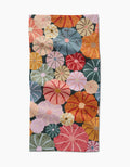 The Gorgeous Gourds towel by Rebecca Bobko is ultra-absorbent and features a vibrant pattern of overlapping, stylized flowers in orange, red, pink, yellow, blue, and green on a dark background.