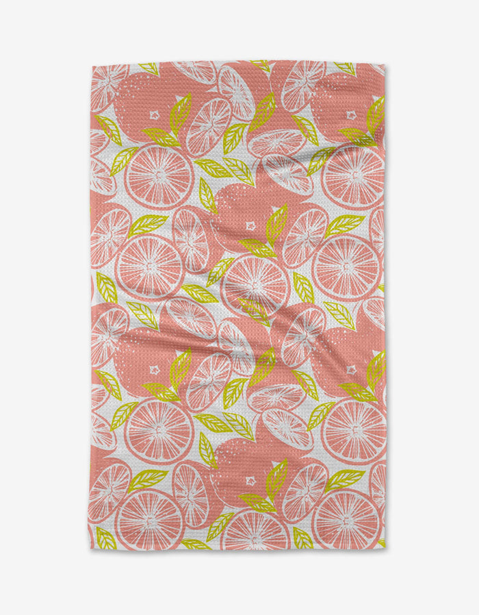 The Elisabeth Wing Grapefruits tea towel is rectangular, made from recycled materials, and features a repeating pattern of pink grapefruit slices with green leaves on a white background. The fabric may have a slightly wrinkled look.