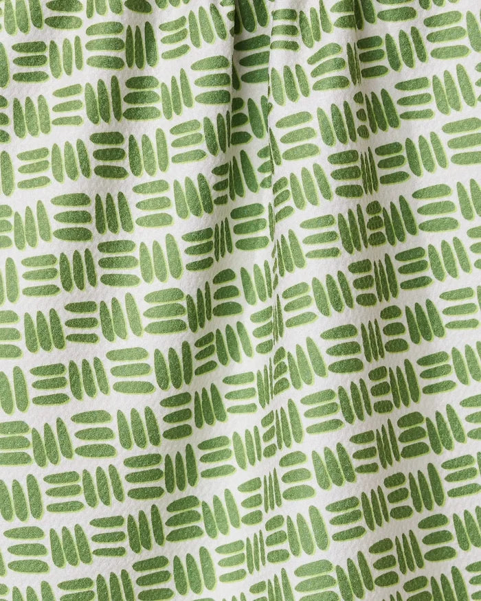 A close-up of the GEOMETRY Grass Hatch tea towel shows its ultra-absorbent white fabric with a repeating pattern of short green hand-drawn lines and ovals in horizontal rows, creating gentle folds and subtle shadows.