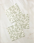 Three Gravenstein Apple napkins by Ash Cascade, made from recycled materials, feature a green leafy fruit pattern and are arranged with overlap on a light marble surface.