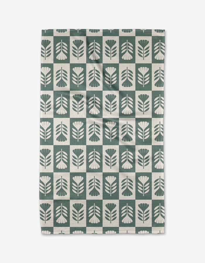 The Green Flower Patch tea towel by Charlie Rowan Designs features a grid of stylized green and white flowers and leaves. Crafted from Geoweave fabric, it blends modern style with superior absorbency.