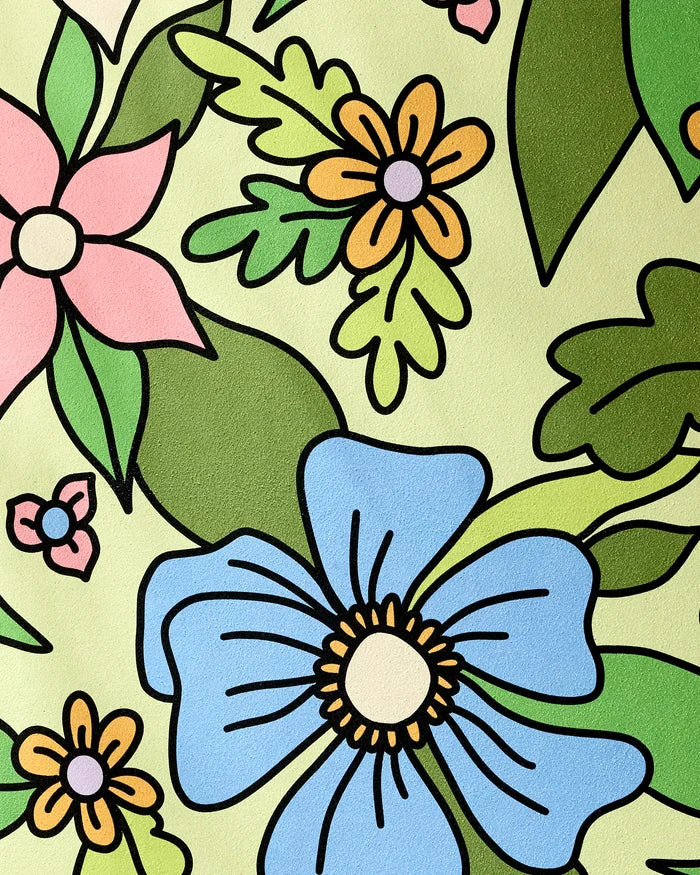 The GEOMETRY "Green Flowers" yoga towel features a bold, cartoon-style floral pattern with large blue, pink, and yellow flowers and green leaves on a light yellow background, outlined in black for extra flair.