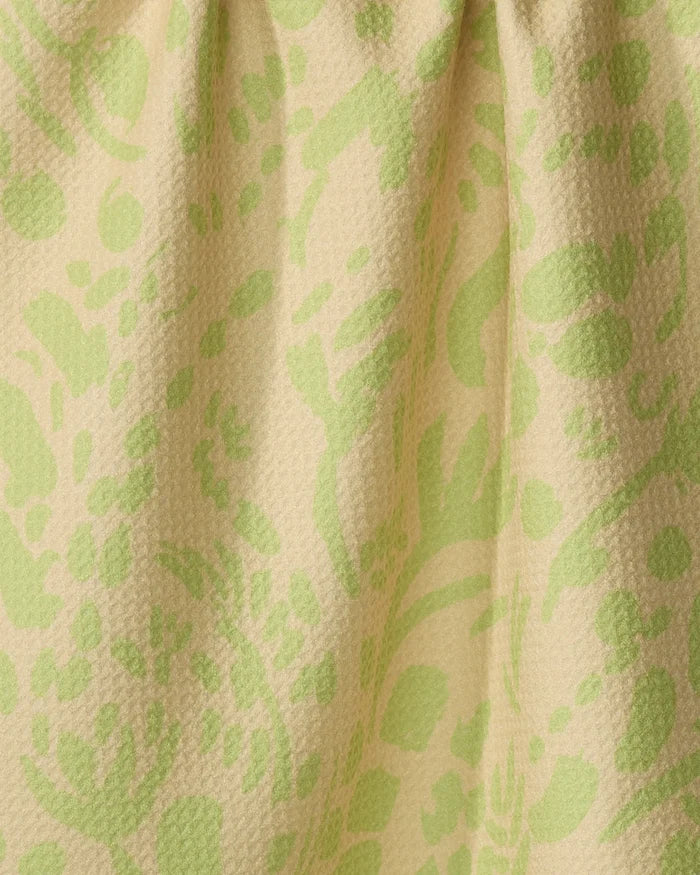 Close-up of Sareka Unique’s Green Spring tea towel, featuring a yellow-beige background with light green floral patterns. Made from recycled materials, the fabric is slightly gathered at the top.