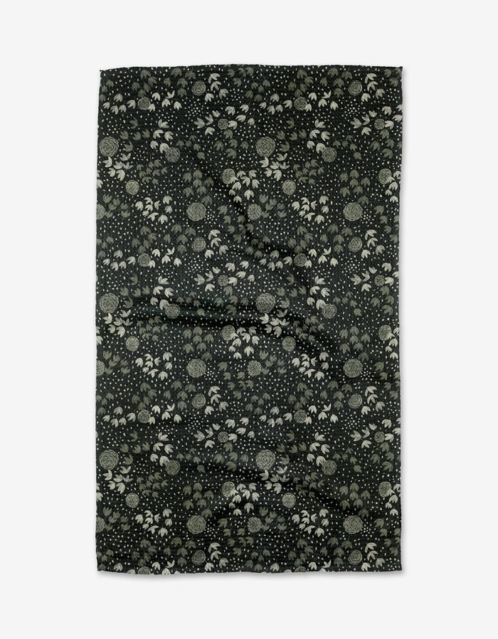 The Green Winter Petal by Katie OShea is a rectangular black recycled kitchen towel with a dense floral and leaf pattern in light gray and white, displayed flat on a white background.