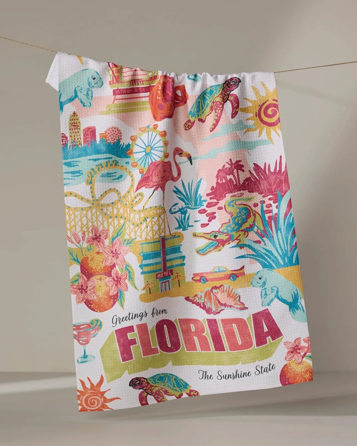 The Geometry "Greetings From Florida" tea towel, crafted from recycled materials, showcases vibrant Florida motifs—flamingos, turtles, citrus, beaches, hotels—and bold “Greetings from FLORIDA The Sunshine State” lettering.