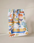 The Geometry Greetings From Idaho Kitchen Tea Towel hangs on a line, showcasing Idaho-themed wildlife, flowers, and scenery in colorful Geoweave fabric with bold yellow text: Greetings from IDAHO The Gem State.
