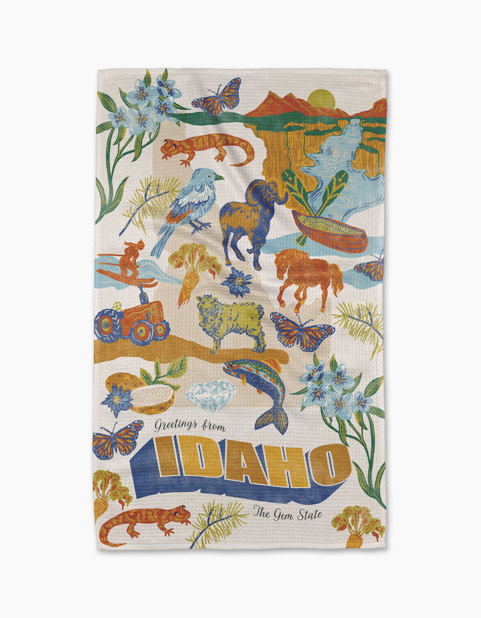 The Geometry Greetings From Idaho kitchen towel showcases vibrant wildlife, flowers, and landscapes, with "Greetings from Idaho" and bold yellow "IDAHO" letters. Made from recycled materials for eco-friendly style.