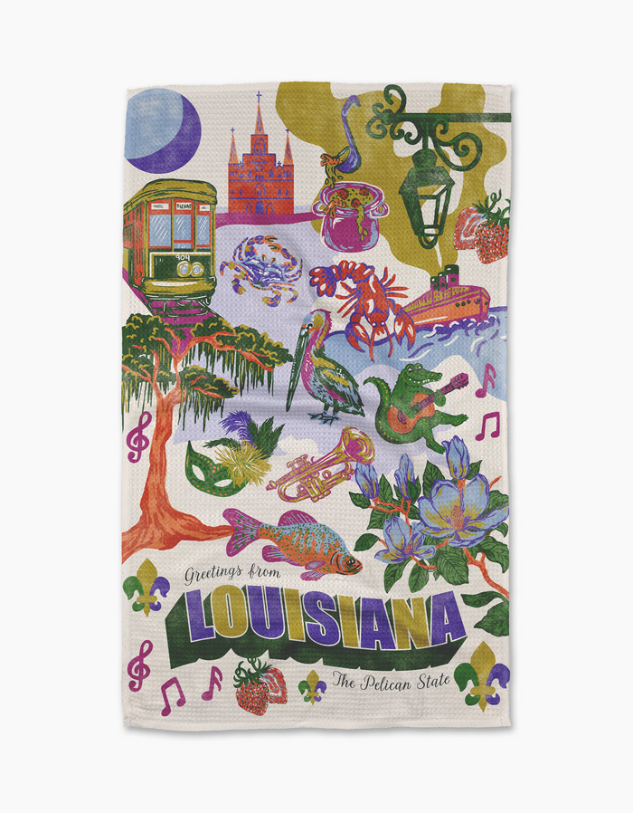 The Geometry “Greetings From Louisiana” towel features a vibrant illustration of iconic local images—trolley, crawfish, alligator, pelican, jazz instruments, Mardi Gras masks, food, flowers—plus “Greetings from LOUISIANA The Pelican State.”.