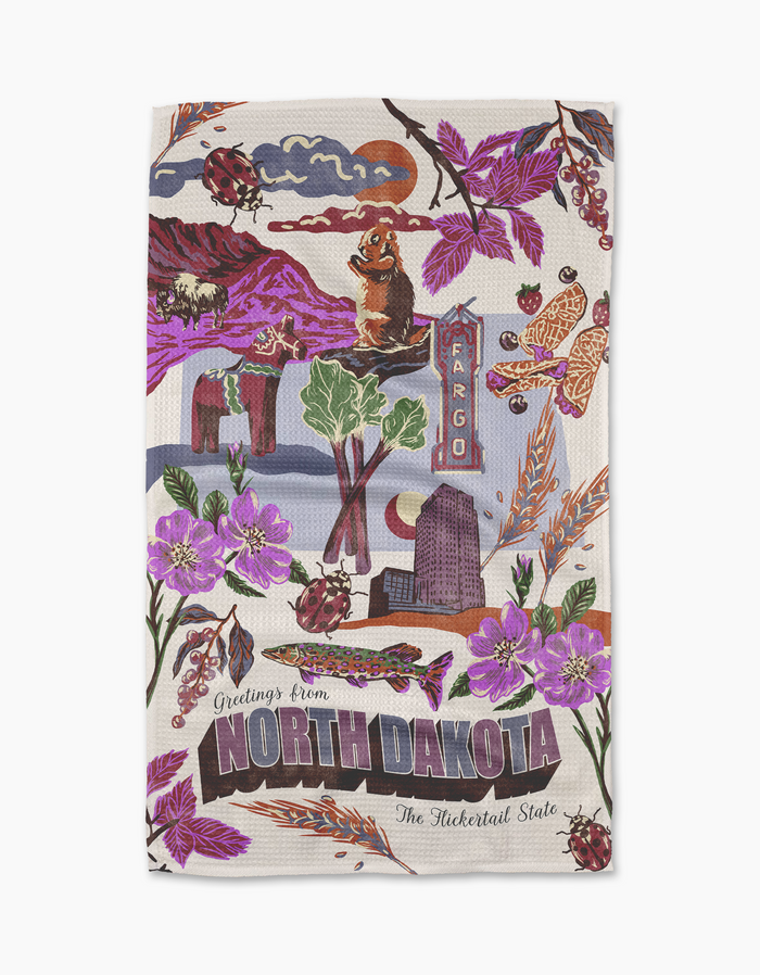The Geometry "Greetings From North Dakota" towel features vibrant illustrations of state symbols—flowers, ladybugs, prairie dog, Fargo sign, bison—and the phrase "Greetings from North Dakota." Made from recycled materials.
