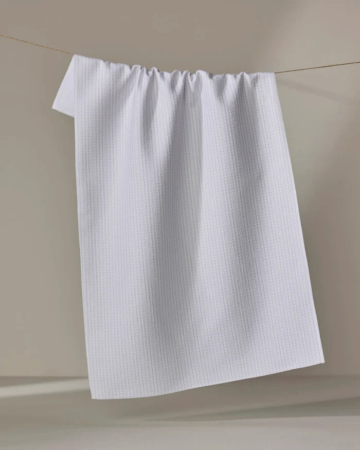 The Grey Salt towel by Kailee Wright, featuring a textured quick-dry design, hangs neatly on a clothesline against a softly lit beige background.