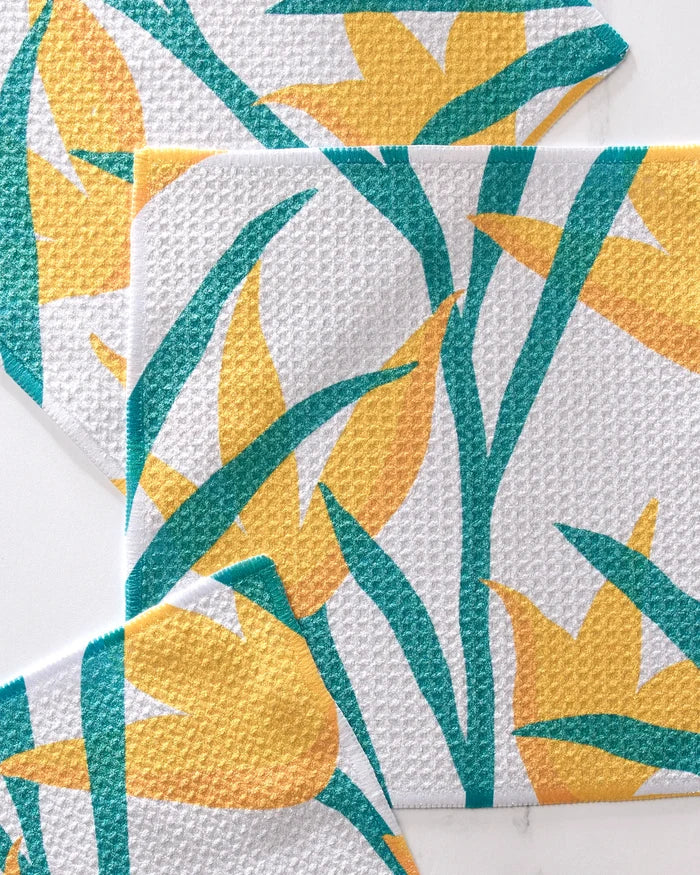 Three white GEOMETRY "Growth" napkins with a textured surface, each featuring a yellow tulip and green leaves pattern, overlap on a flat surface. This eco-friendly, spring-themed set is crafted from recycled materials.