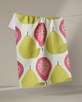 The Lizzie Clark "Guava Groove" recycled kitchen towel, adorned with yellow pears and pink guavas, hangs on a string against a neutral background.