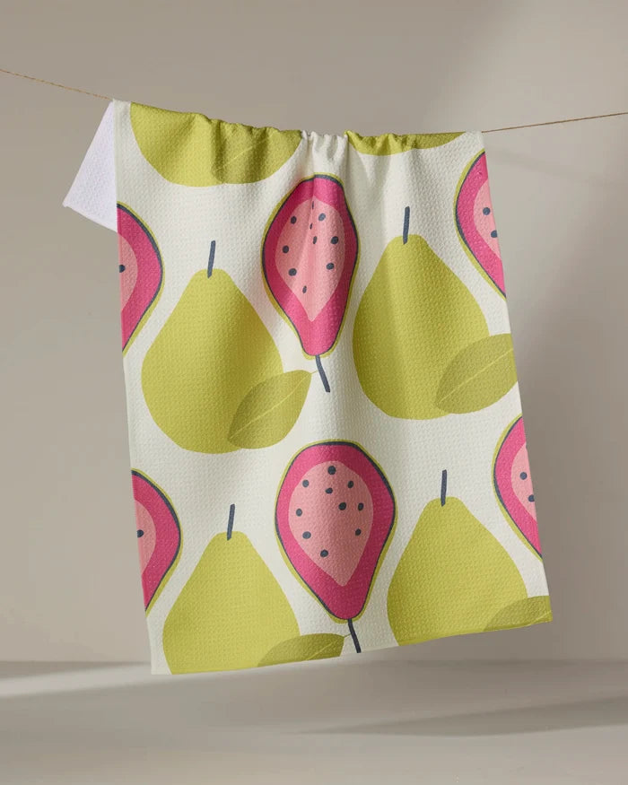 The Lizzie Clark "Guava Groove" recycled kitchen towel, adorned with yellow pears and pink guavas, hangs on a string against a neutral background.