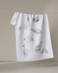 The "Guinea Fowls" tea towel by Taryn Brennan features watercolor guinea fowl illustrations on a plain light background. Made from quick-drying recycled materials, it hangs perfectly for display or everyday use.