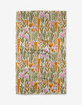 The Gwendolyn tea towel by Amy MacCready features orange carrots, brown and green leaves, and pink flowers on white, crafted from recycled materials.