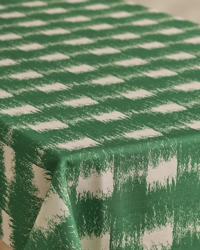 The Geometry Hairy Check Green tablecloth, featuring a green and white checkered distressed pattern, is stain-resistant and drapes elegantly over rectangular tables.