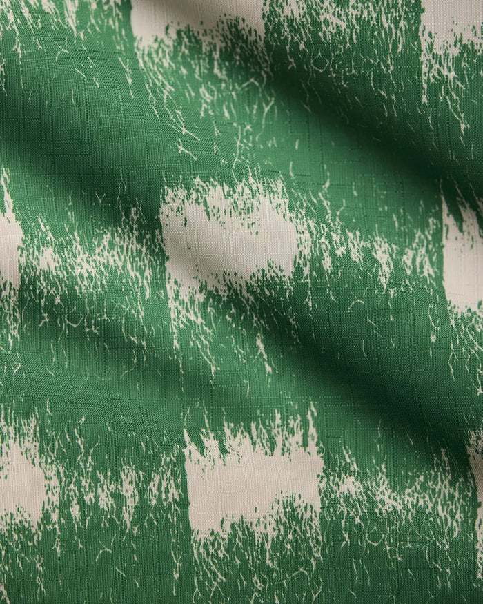 A close-up of Geometry’s Hairy Check Green table runner fabric shows its green and white rough brushstroke checkered pattern, highlighting the slight creases and texture.
