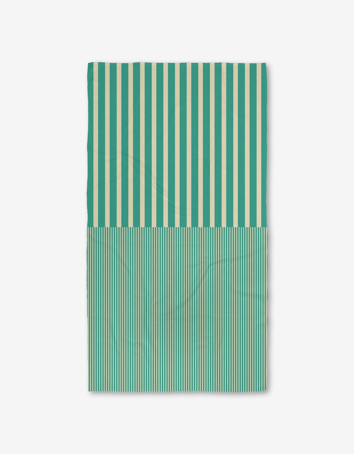 The GEOMETRY Half and Half is a rectangular Luxe Bath Towel featuring vertical teal and cream stripes—wide on top, thin below—made from ultra-absorbent recycled materials, shown on a plain white background.