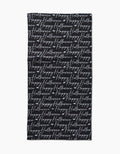 The Geometry Halloween Script Black towel is a black rectangular bar towel with “Happy Halloween” written repeatedly in white cursive across its surface.