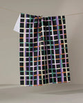The Happy Plaid tea towel by Claire Iglesias features a vibrant green, lavender, peach, white, and orange grid on black—ultra-absorbent and perfect for brightening any kitchen with its colorful design.