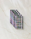 Seven rectangular Claire Iglesias Happy Plaid reusable paper towels with a pastel checkered pattern in pink, purple, green, and orange are arranged in an overlapping row on a light marble-textured surface.
