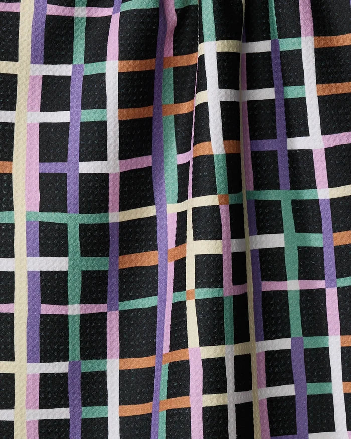 Close-up of the Happy Plaid kitchen towel by Claire Iglesias, made from recycled materials. It features a textured grid pattern in pastel green, purple, pink, white, and tan on black, with the fabric shown draped.