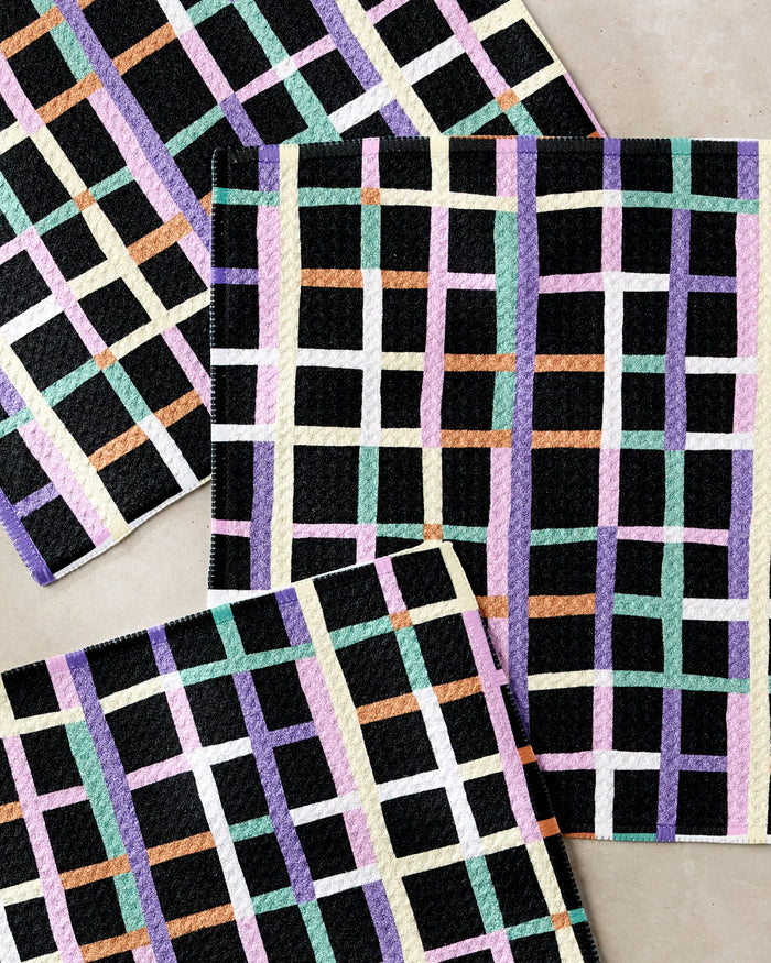 The Happy Plaid dishcloth set by Claire Iglesias includes four rectangular mats with a vibrant pastel grid on black. Made from recycled materials, these super-absorbent towels add color and cheer to your kitchen.
