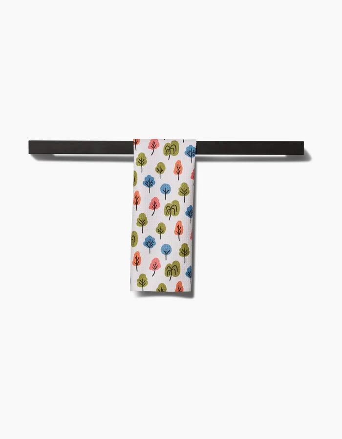 The Kayla Ann Happy Trees Bar Towel, crafted from Geoweave fabric, features a colorful repeating tree pattern and hangs neatly on a black rack against a white background, blending style and function.