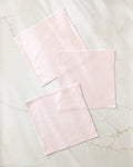 Three Harper Pink textured cloth squares from Kailee Wright's super-absorbent dishcloth set are neatly arranged on a white marble surface with light gray and beige veining.