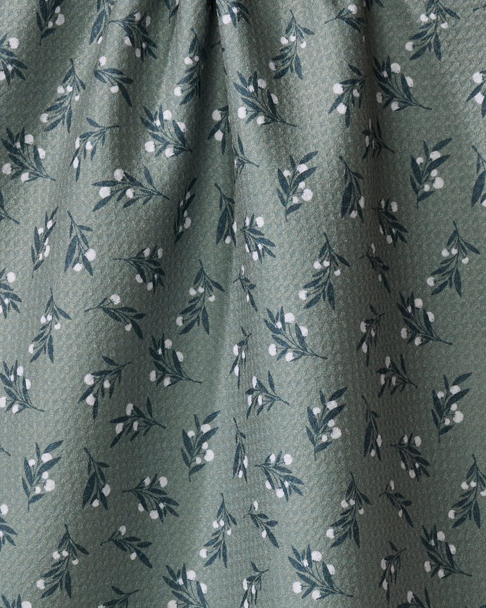 The Harvest Berries dish towel by Charlie Rowan Designs features green fabric with a subtle texture and an absorbent surface, decorated with small dark green leafy branches and white berry clusters.