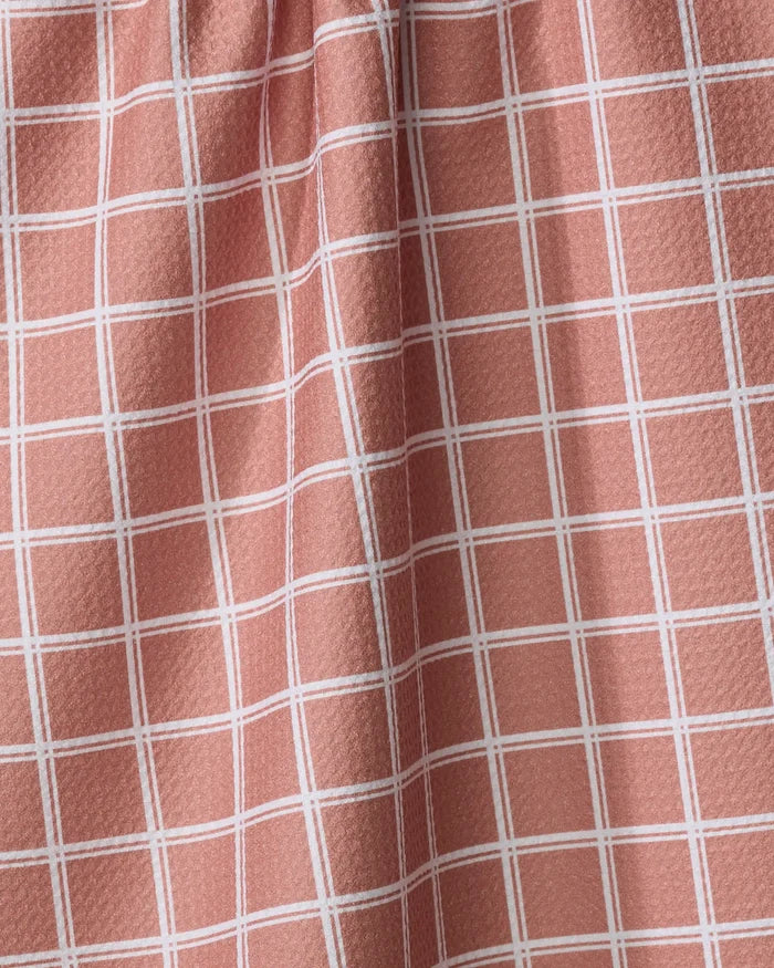 A close-up of the Harvest Plaid tea towel by Charlie Rowan Designs shows its pink and white grid pattern, textured surface, and gentle folds that create subtle shadows and highlights.