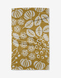 Harvest Toss by Lizzie Clark is a mustard yellow Tea Towel made from Geoweave™ fabric with recycled materials, featuring a white botanical and pumpkin pattern. The slightly wrinkled towel is shown on a white background.