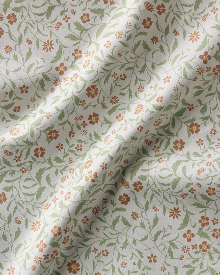 A close-up of Danelys Sidron’s Hawthorns napkins—cream-colored, eco-friendly table linens patterned with small orange flowers and green leaves. The recycled fabric is gently wrinkled, forming soft folds and shadows.