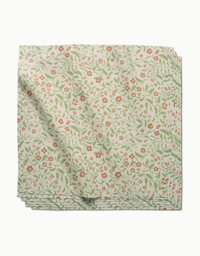 A neatly folded stack of cream-colored Danelys Sidron Hawthorns Geosuede dinner napkins, featuring a green vine and red floral pattern, displayed on a white background.