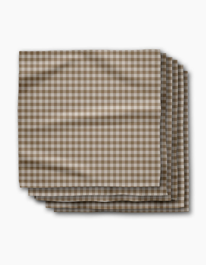 Four folded Geometry Hazel Gingham reusable napkins, featuring a brown and white checkered pattern, are neatly stacked on a white background with gentle creases.