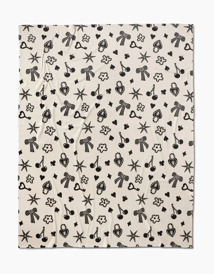 Heart Locket by Geometry is a cream-colored, silky-soft fabric adorned with evenly spaced black bows, starbursts, cameo profiles, hearts, keys, cherries, and flowers for a whimsical touch.