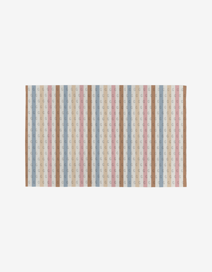 The Heartbreaker rug by Hufton Studio is a rectangular design with vertical stripes in pastel blue, pink, beige, and brown, featuring a subtle repeating G pattern, crafted from eco-friendly post-consumer recycled materials.
