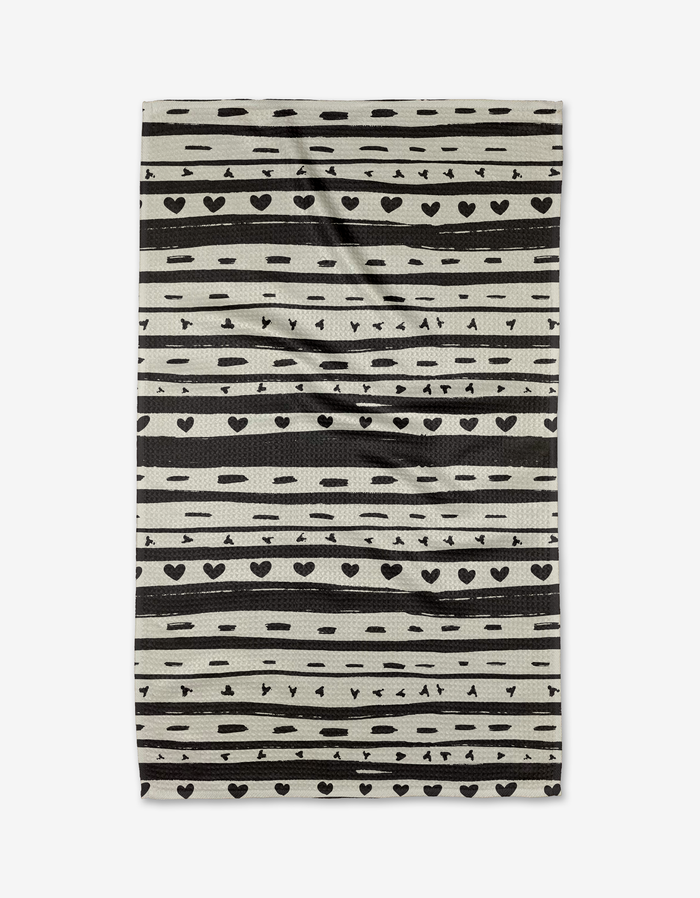 The Danelys Sidron Heartstring tea towel is rectangular and beige, made from recycled materials with black stripes, dots, hearts, and triangles in a repeating pattern. Slightly wrinkled, it is displayed on a white background.