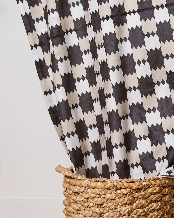 The Highland Lullaby by Geometry is a soft throw blanket with a black, white, and beige geometric pattern, draped over a woven basket to highlight its bold design.