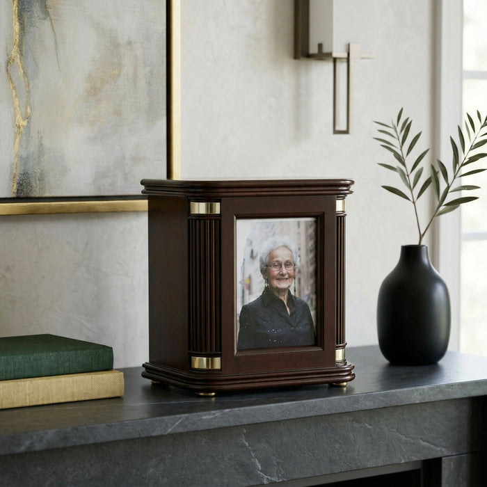 Decorative urn with a photo of an elderly woman on a shelf with books and a vase.