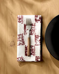 The Geometry Horse Check Cream recycled dinner napkin is folded under a fork with a wooden handle, next to the edge of a black plate on a light wooden table.